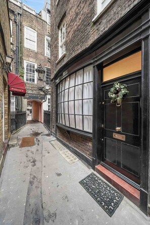 Une ruelle étroite avec une porte noire, un auvent rouge et un bâtiment en briques doté d’une fenêtre.