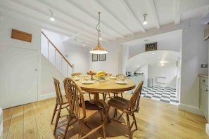 A dining area with a wooden table and chairs, a hanging light fixture, and a staircase leading to another level.
