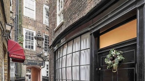 A narrow alleyway with a black door and a window with a grid pattern. There is a red awning above a sign that reads "Bedfordbury." A doormat is placed at the door's base. - Stunning haven for 6 guests in the heart of London (London)