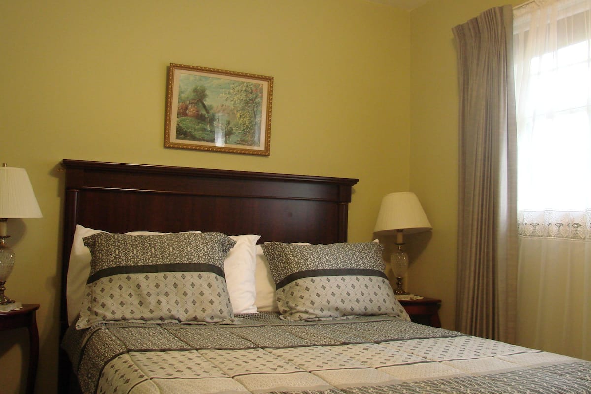A neatly made bed with patterned bedding, a framed picture on the wall, and two bedside lamps.
