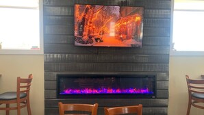 A living room with a fireplace, a television mounted above it, and two wooden chairs.