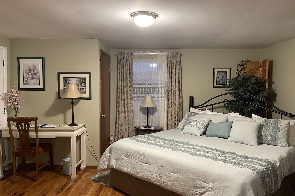 A bedroom with a bed, a desk, a chair, a lamp, and a window with curtains.