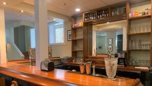 A bar area with a wooden counter, bar stools, a cash register, and a large mirror above the counter.