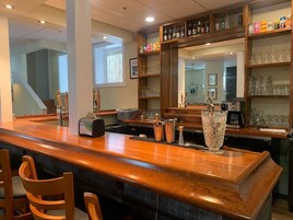 A bar area with a wooden counter, bar stools, a cash register, and a large mirror above the counter.