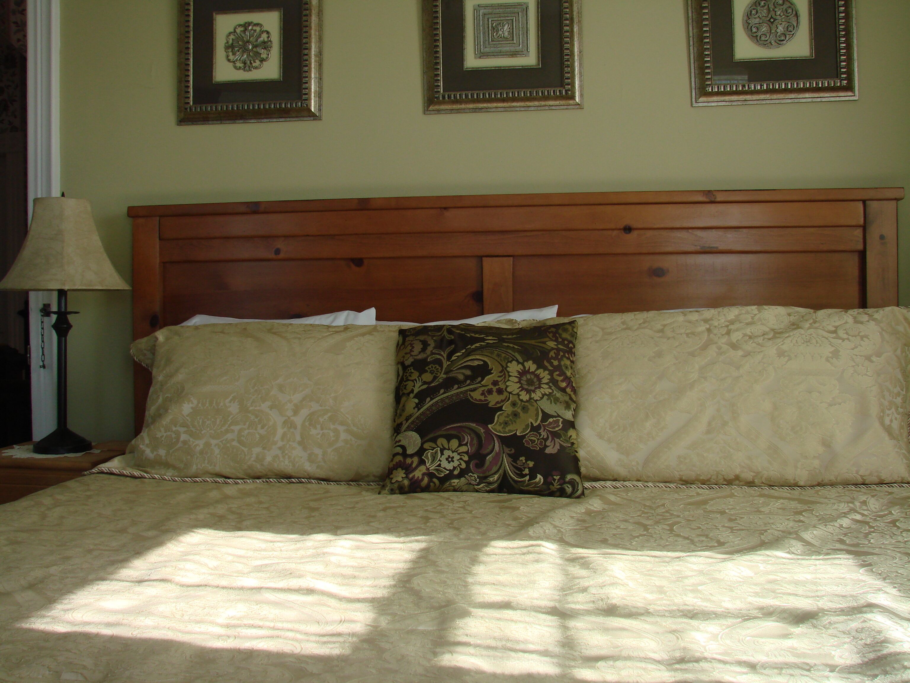 A bed with a wooden headboard, two patterned pillows, and a lamp on a nightstand.
