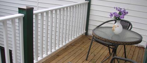 A wooden deck with a white railing and green posts, a round table with chairs, and a vase with purple flowers.