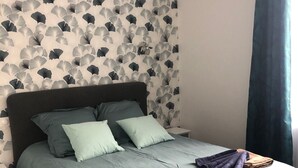 Un lit bien fait, avec une couverture grise, deux oreillers et des serviettes pliées.