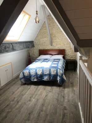 A bedroom with a sloped ceiling, a wooden bed, a quilted bedspread, and a stone wall.