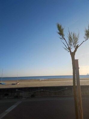 A beach with a clear sky, a wooden post, and boats on the sand.