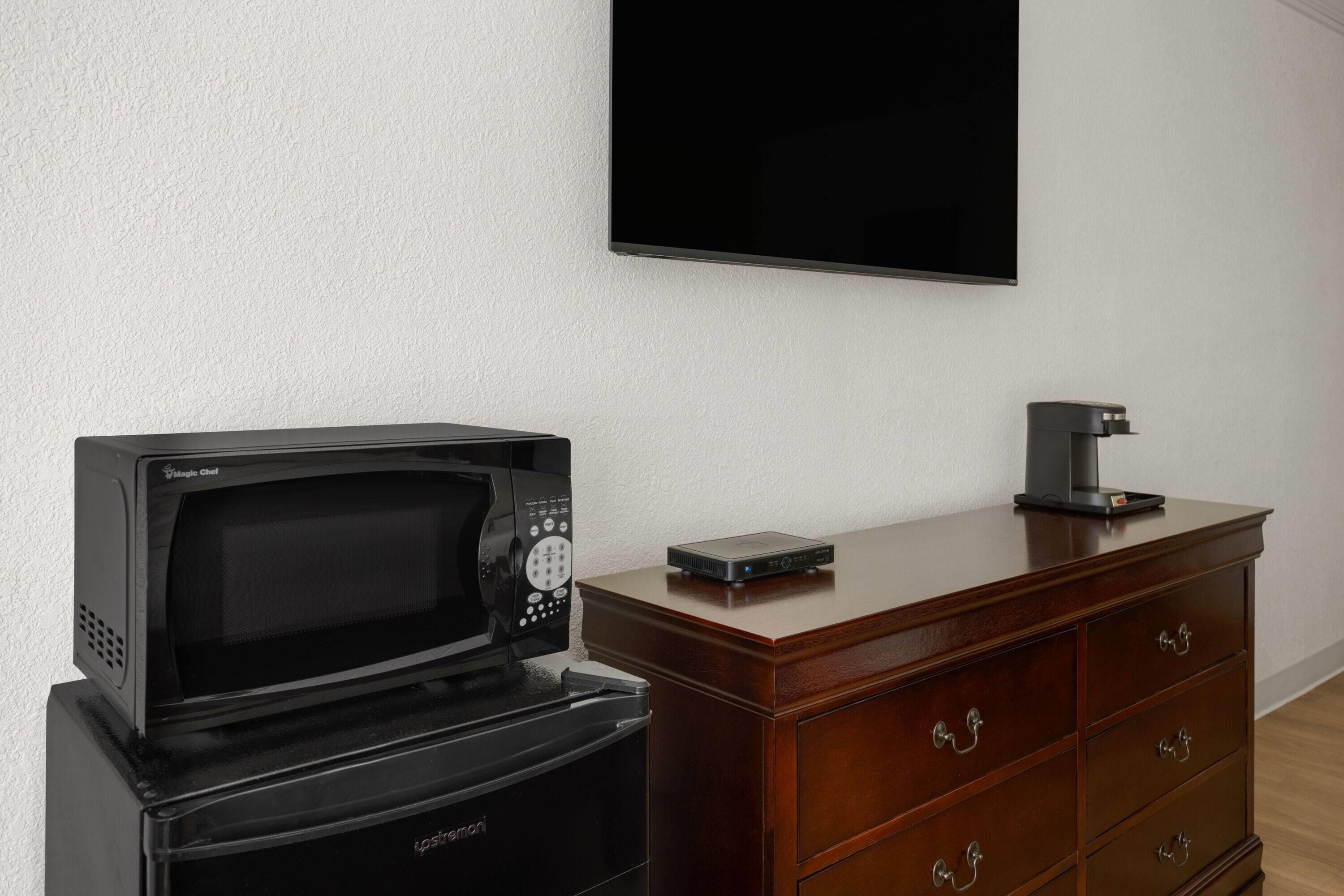 Una cocina con microondas, cafetera y televisor de pantalla plana montado en la pared.
