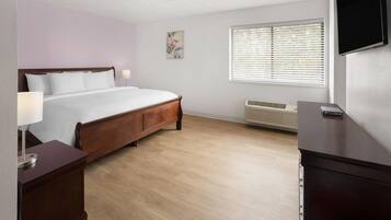 A hotel room with a wooden bed, bedside lamps, a flat-screen TV, a window with blinds, and a wall-mounted air conditioner.