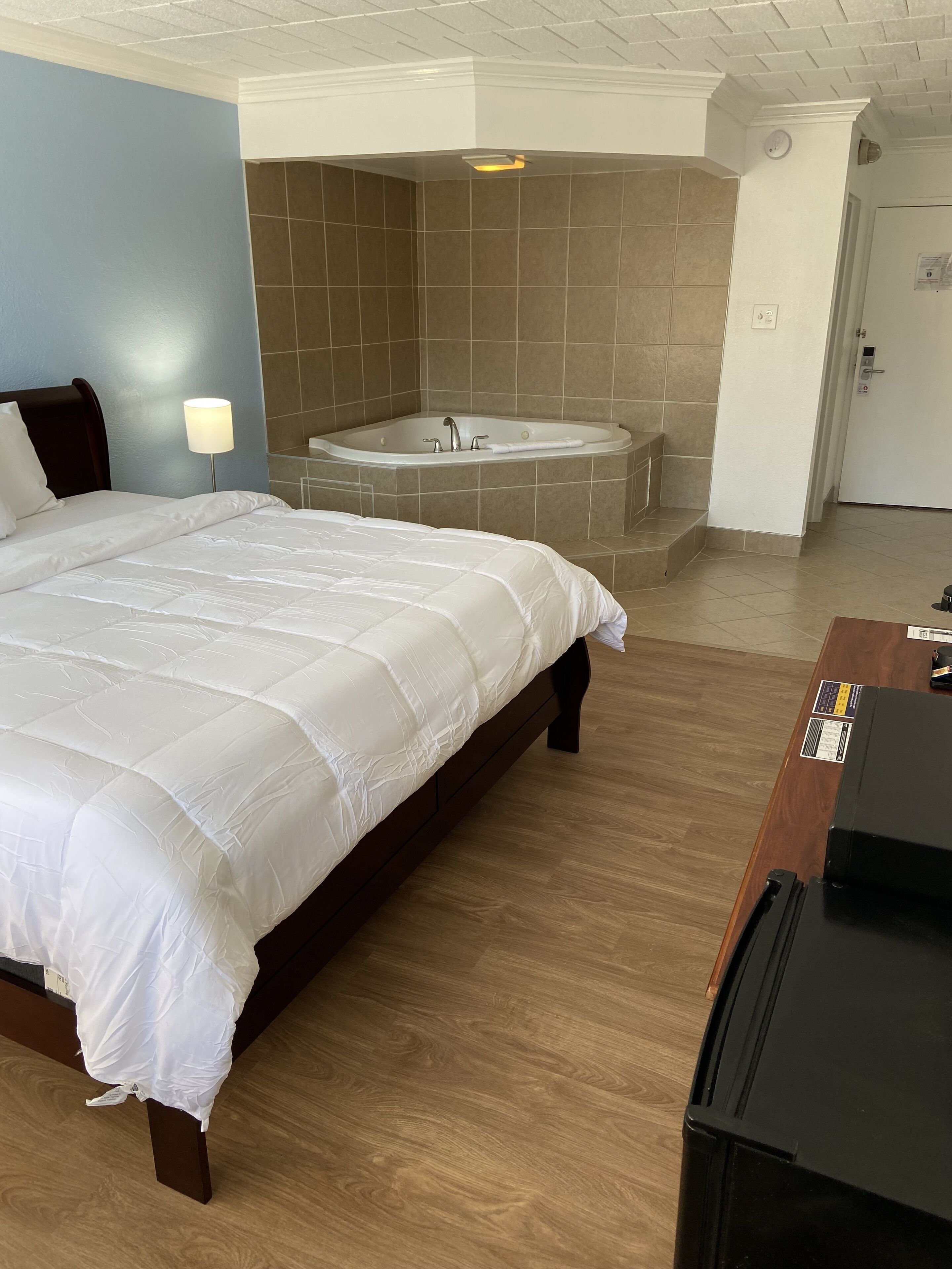 Une chambre d’hôtel avec un grand lit, un plancher en bois, une salle de bain avec baignoire et un bureau équipé d’un ordinateur.