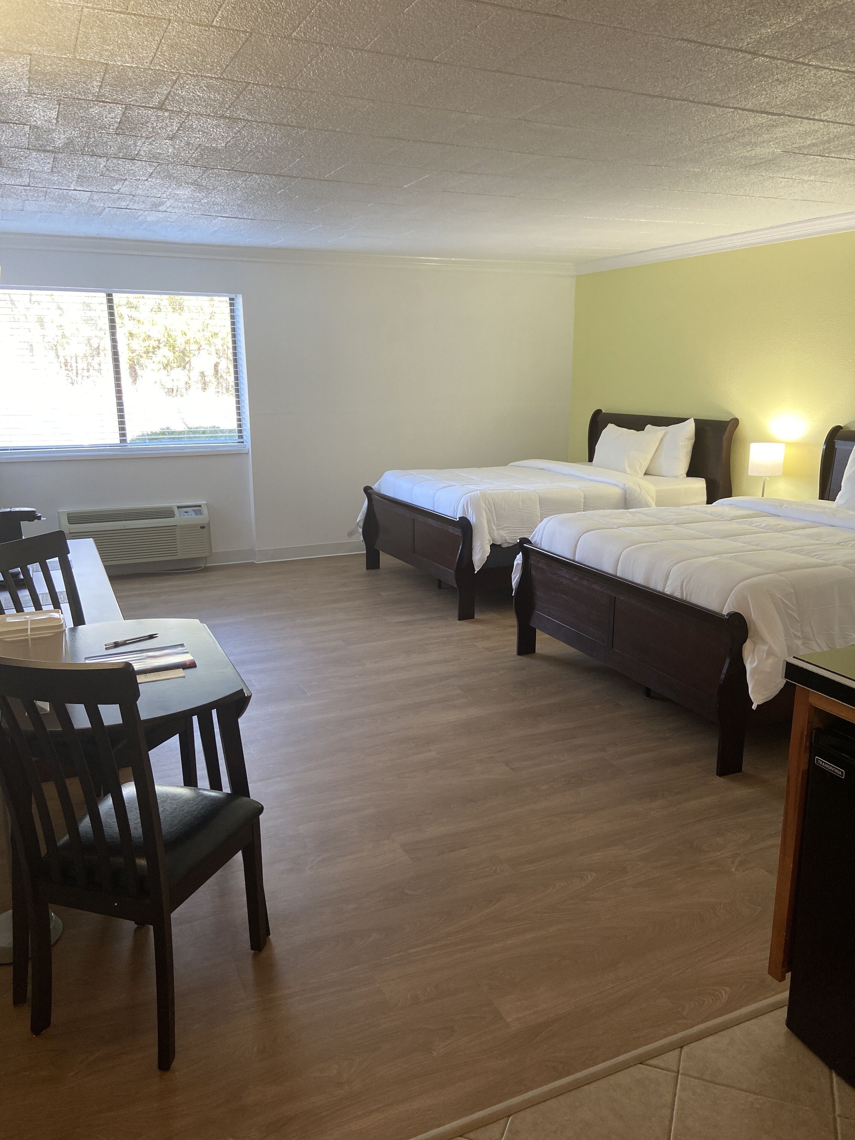 A hotel room with two beds, a wooden dining table, and a window with blinds.