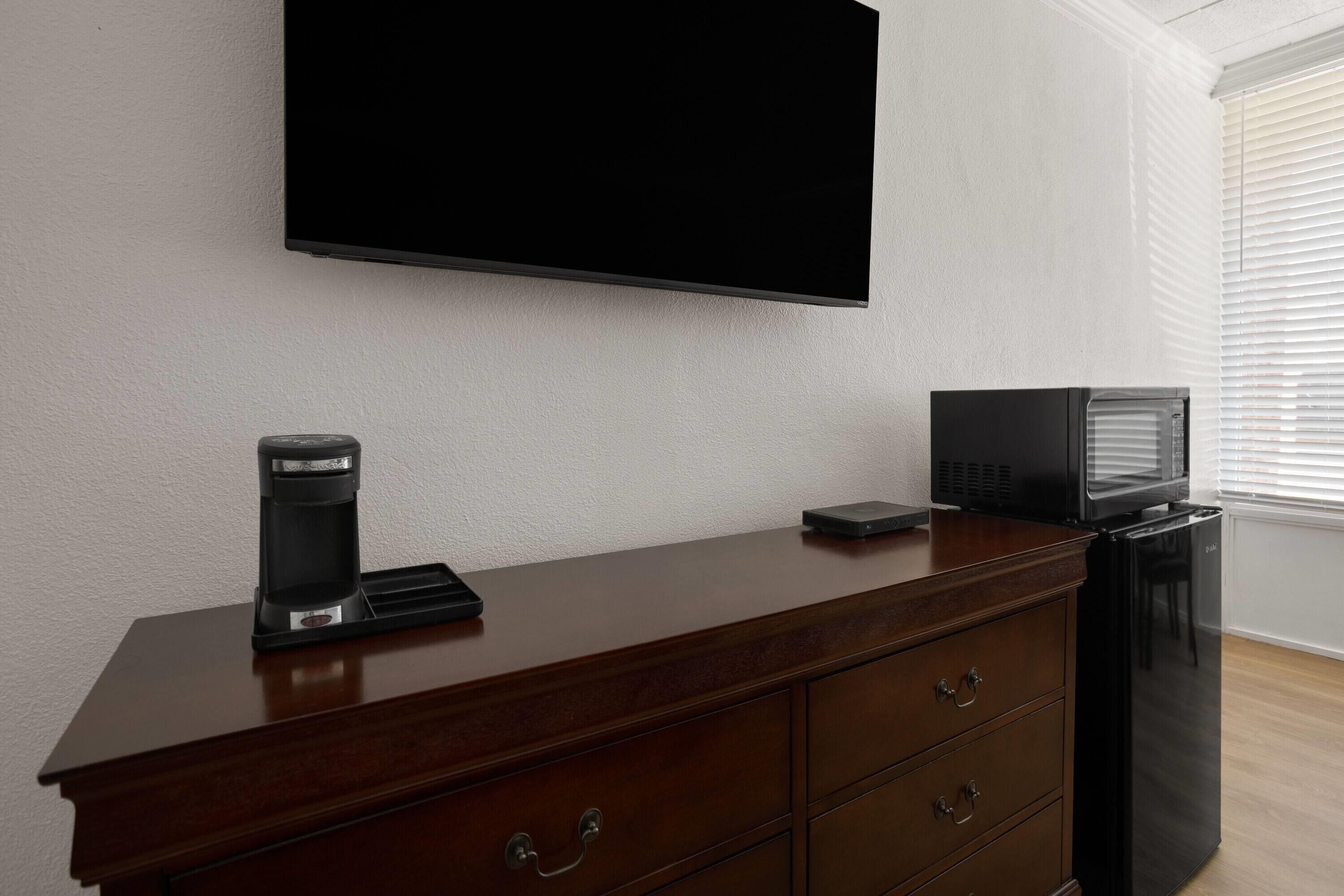 Una habitación moderna con una televisión de pantalla plana montada en la pared, una cafetera, un microondas y un refrigerador sobre un aparador de madera.