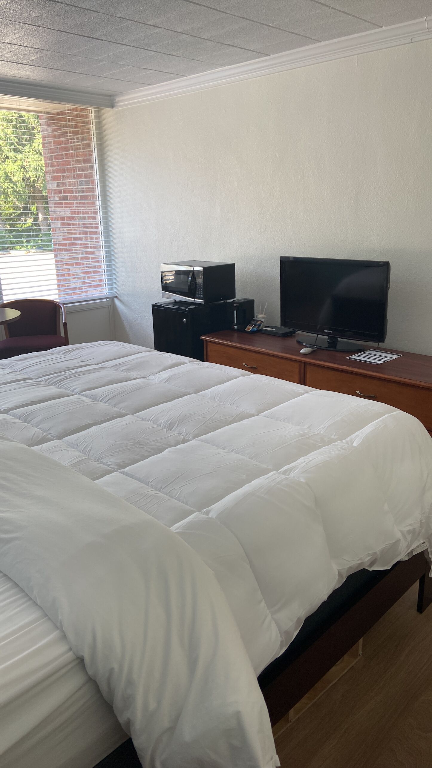 Habitación de hotel con una cama grande, un televisor sobre un aparador de madera y una ventana con persianas.