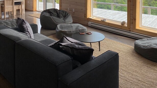 Een ruime woonkamer met een grote bank, een salontafel en een relaxfauteuil. Er zijn meerdere ramen met uitzicht op de omgeving.