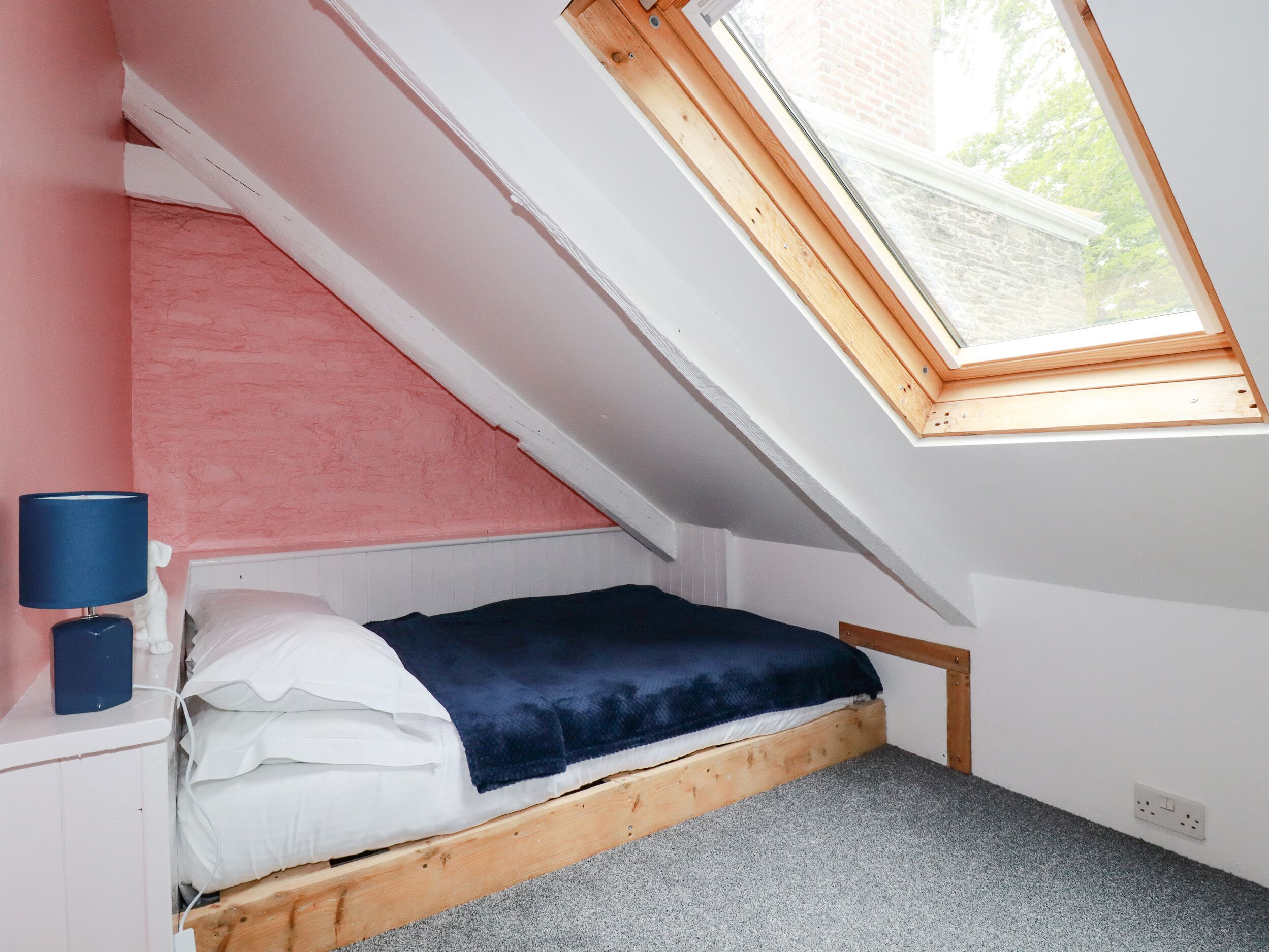 A small, slanted room with a single bed, a skylight, and a bedside lamp.