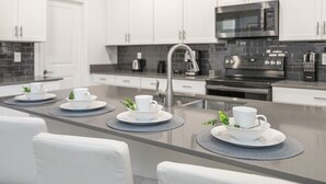 Une cuisine moderne avec des armoires blanches, un îlot central en acier inoxydable et un four à micro-ondes encastré.
