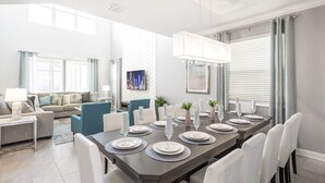 Un espace repas moderne avec une longue table dressée pour six personnes, entourée de chaises blanches.