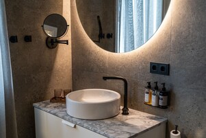 Un baño con un lavamanos blanco, un espejo redondo y una lámpara en la pared.
