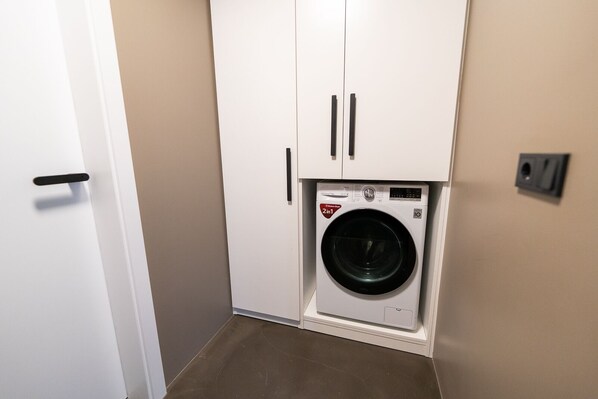 A compact laundry room with a front-loading washing machine, white cabinets, and a door.