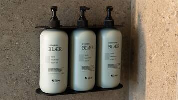 Três frascos de produtos Bluerose sobre uma prateleira preta contra uma parede texturizada.