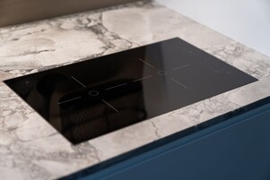A kitchen with a built-in induction cooktop and a marble countertop.