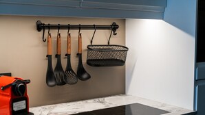 A kitchen with a marble countertop, a black induction cooktop, and a hanging rack with wooden-handled utensils and a black mesh basket. - Keflavik Luxury Apartments (Reykjanesbær)