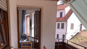 A wooden dining table with chairs, a view of a building through an open door, and a balcony with a railing. - 3,5 Zimmer Ferienwohnung am Fuße der Schwäbischen Alb Balingen (Balingen)