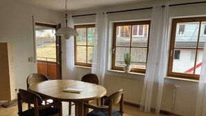 A dining area with a round wooden table, four chairs, a hanging light fixture, and large windows with curtains. - 3,5 Zimmer Ferienwohnung am Fuße der Schwäbischen Alb Balingen (Balingen)