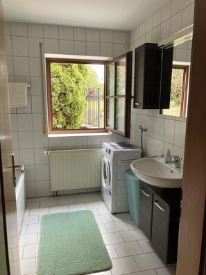 A compact bathroom with a built-in washing machine, a sink, and a window with a view of greenery. - 3,5 Zimmer Ferienwohnung am Fuße der Schwäbischen Alb Balingen (Balingen)