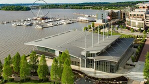 A modern building with a curved roof and large windows, situated near a waterfront with a Ferris wheel and boats. - Close to DC excellent location (Temple Hills)