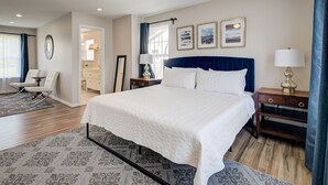 A hotel room with a large bed, a ceiling fan, a nightstand with a lamp, a dresser, and a seating area with a chair and a table. - Close to DC excellent location (Temple Hills)