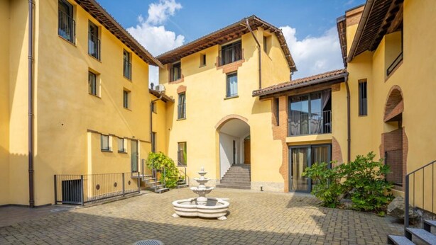 A courtyard with a fountain, yellow buildings, and a staircase leading to an entrance. - Parco Vira Apartments (Porza)