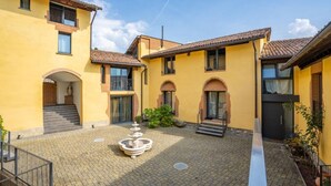 A courtyard with a fountain, a staircase, and a building with yellow walls and tiled roofs. - Parco Vira Apartments (Porza)