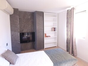 A bedroom with a bed, a TV, a bookshelf, and a window with curtains. - Parco Vira Apartments (Porza)