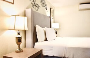 A hotel room with a bed, two bedside lamps, a decorative wall piece, and a framed picture.