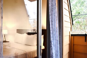 Relax in this serene bedroom with a comfortable bed, nightstand, and a large window offering a peaceful view of the outdoors.