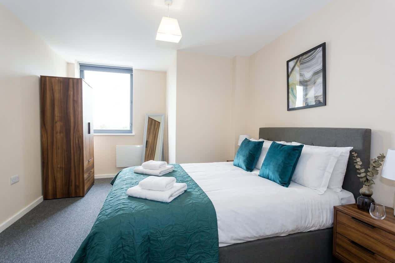 Une chambre d’hôtel comprenant un lit, une table de chevet, une commode, une armoire, une fenêtre et un tableau au mur.
