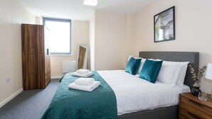 Una habitación de hotel con cama, mesita de noche, armario, ventana y un cuadro en la pared.