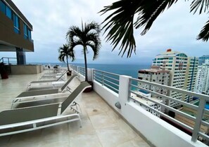 A balcony with metal chairs, a palm tree, and a view of the ocean and buildings. - Oceanfront | 3 bedrooms | Spectacular view | Wi-Fi. Parking!! (Salinas)