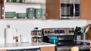 Una cucina moderna con piano cottura in acciaio inossidabile, forno a microonde e un set di stoviglie verdi sugli scaffali.