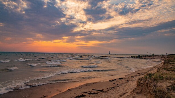 A beach with waves, a lighthouse, and a sunset.