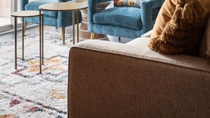 A modern living room with a blue sofa, a beige sofa, and a coffee table. There is a patterned rug on the floor.