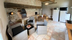 A rustic kitchen with exposed brick walls, wooden beams, wicker furniture, and a stone fireplace.
