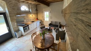 A rustic kitchen with stone walls, wooden beams, a dining table with chairs, a washing machine, and a sofa.
