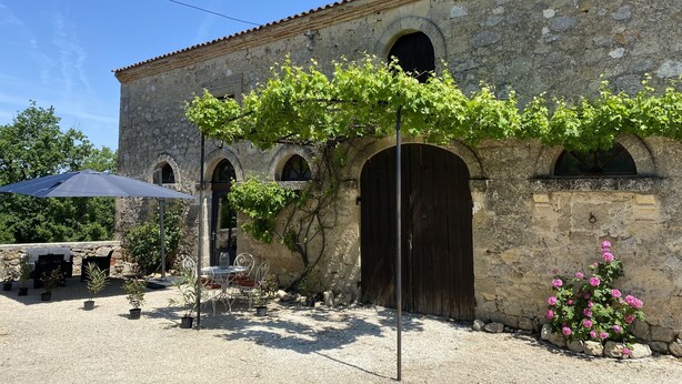 A stone building with arched windows and a covered patio area with a table and chairs.