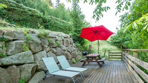 A wooden deck with two lounge chairs and a red umbrella, surrounded by a stone wall and lush greenery. - Les Pistes de Ventron (Ventron)