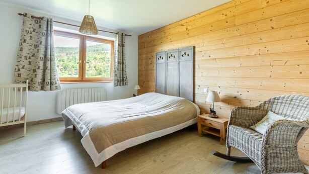 A bedroom with a bed, a crib, a wicker chair, and a wooden wall. - Les Pistes de Ventron (Ventron)