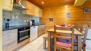 A kitchen with wooden cabinets, a stove, and a dining table with chairs. - Les Pistes de Ventron (Ventron)